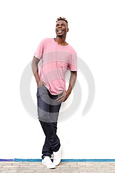 Full length cool young african man leaning against white wall looking away and smiling