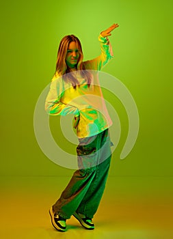 Full length portrait of cute child, girl, student dancing and looking at camera in mixed colors neon light against