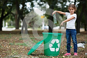 A little child putting the garbage in a green recycling bin on a blurred natural background. Ecology pollution concept.