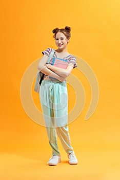 Full length portrait of a cute smiling girl holding books isolated on the yellow background