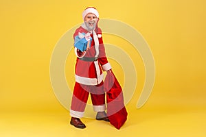 Full length portrait of elderly man with gray beard wearing santa claus costume standing with red