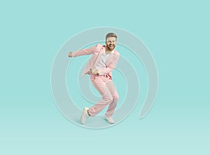 Full length portrait of excited dancing young man in pastel pink trendy suit