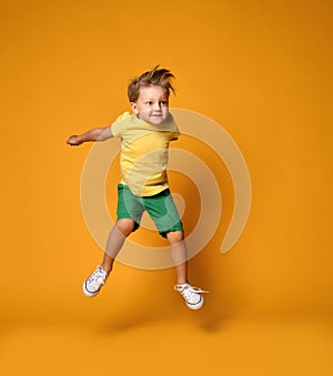 Full length portrait of an excited young boy jumping leaping in green shorts over yellow