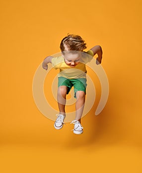 Full length portrait of an excited young boy jumping leaping in green shorts over yellow