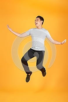 Full length portrait of an excited young man in white t-shirt jumping while celebrating success isolated over orange background