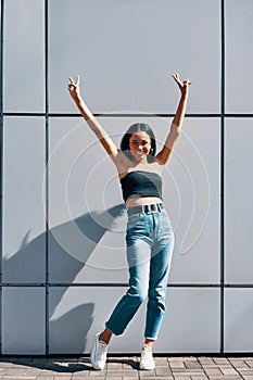 Full length portrait of fashionable young black woman with arms raised showing peace sign