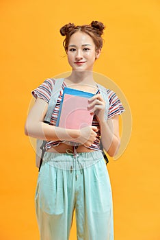 Full length portrait of a female student with a backpack and books isolated on yellow background