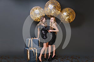 Full-length portrait of graceful girl with trendy hairstyle touching gift box and laughing. Studio photo of two ecstatic