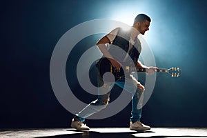 Full length portrait of guitarist in denim playing electric guitar, with dynamic backlight and smoke creating artist