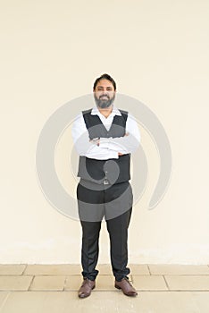 Full length portrait of handsome bearded Indian businessman against plain background