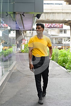 Full length portrait of handsome black African man wearing yellow t-shirt outdoors in city during summer and walking
