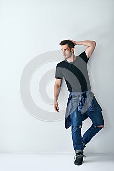 Full length portrait of handsome stylish man leaning at white wa