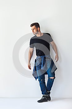 Full length portrait of handsome stylish man leaning at white wa