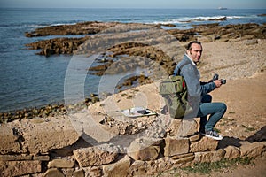 Full length portrait of a handsome traveler man in casual denim, drinking hot drink while taking a coffee break by sea