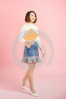 Full length portrait of a happy asian businesswoman holding document while walking isolated over pink background