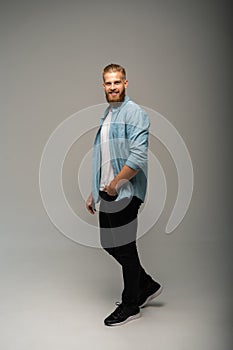 Full length portrait of a happy casual man standing isolated on a gray background.