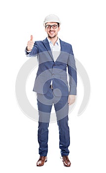 Full length portrait of happy cheerful businessman engineer wearing protective helmet smiling shows thumb up positive gesture
