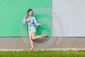 Full length portrait of happy excited beautiful woman in casual jeans denim style in summertime standing near green and light blue