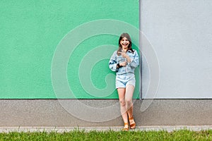 Full length portrait of happy excited beautiful woman in casual jeans denim style in summertime standing near green and light blue