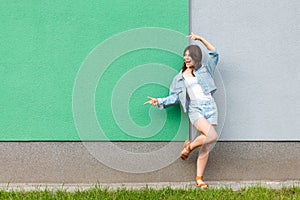 Full length portrait of happy excited beautiful woman in casual jeans denim style in summertime standing near green and light blue