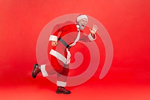 Full length portrait of happy excited elderly man in santa claus costume standing looking at camera