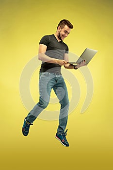 Full length portrait of happy jumping man with gadgets on yellow background