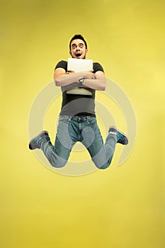 Full length portrait of happy jumping man with gadgets on yellow background