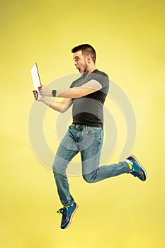 Full length portrait of happy jumping man with gadgets on yellow background