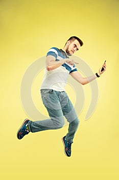 Full length portrait of happy jumping man with gadgets on yellow background