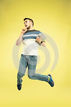 Full length portrait of happy jumping man with gadgets on yellow background