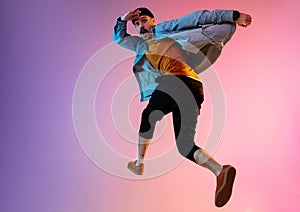 Full length portrait of happy jumping man in neon light and gradient background