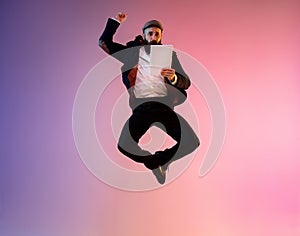 Full length portrait of happy jumping man in neon light and gradient background