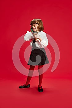 Full-length portrait of happy little girl in black shirt and white blouse, talking on mobile phone and laughing against