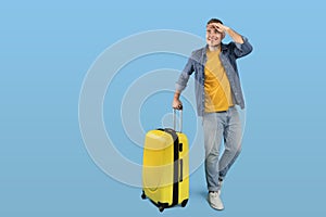 Full length portrait of happy male traveler with luggage looking at empty space over blue studio background