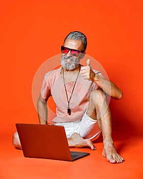 Full length portrait of a happy old man using laptop computer over orange background