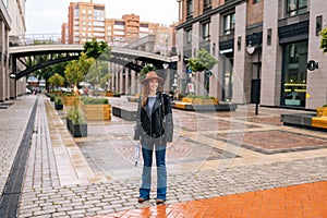 Full length portrait of happy redhead young woman wearing elegant hat standing with folded transparent umbrella on