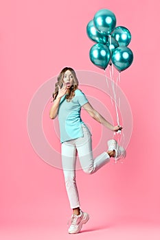 Full length portrait of happy surprised woman with blue balloons in hands on pink background.