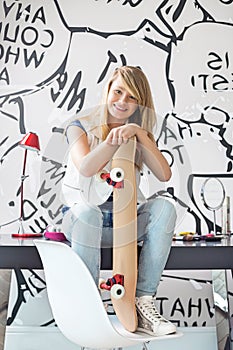 Full-length portrait of happy teenage girl with skateboard sitting on study table at home