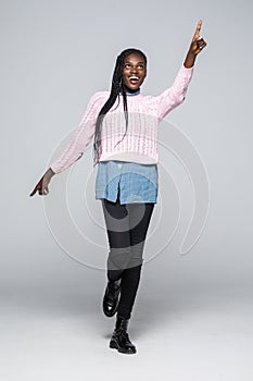 Full length portrait of a happy young african woman jumping and pointing finger at copy space over gray background