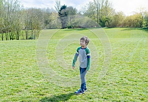 Full length Portrait Happy young boy standing in the park with blurry grass fields and  trees background,Active child looking out