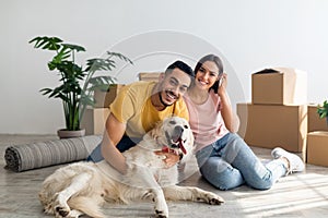 Full length portrait of happy young diverse couple with their dog posing on floor of new home on moving day