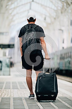 Full length portrait of a happy young man walking with suitcase at train station. Travel concept