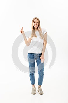 Full length portrait of a happy young woman standing and showing peace gesture with two hands isolated over white