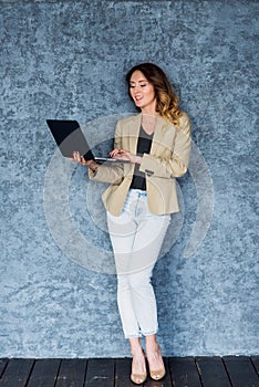 Full length portrait of a happy young woman using laptop over gray background.