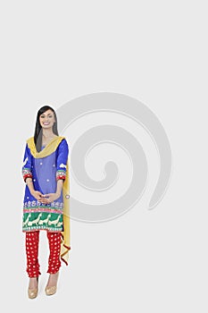 Full length portrait of Indian woman in traditional wear standing over gray background