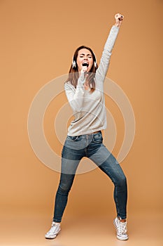 Full length portrait of joyful pretty woman in casual wear holding her smartphone like microphone