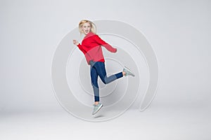 Full length portrait of a joyful young woman jumping and celebrating over gray background