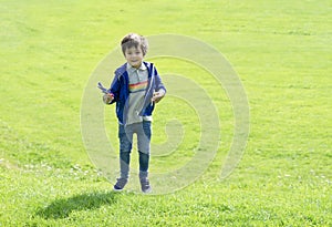Full length portrait kid jumping in the green grass, Cute little boy playing plastic airplane toy, Child having fun playing