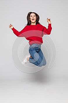 Full length portrait of a laughing woman in red sweater jumping over gray background