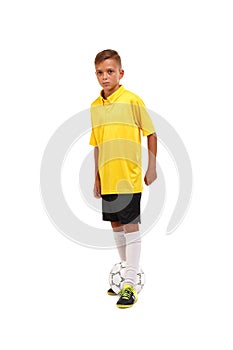 Full-length portrait of a little footballer in a yellow T-shirt, black shorts isolated on a white background.